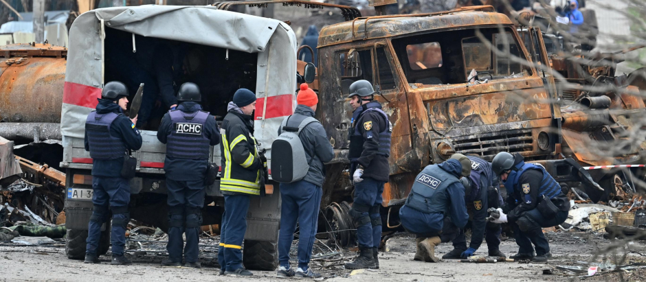 Los ingenieros ucranianos realizan la limpieza de minas entre los vehículos destruidos en una calle de Bucha