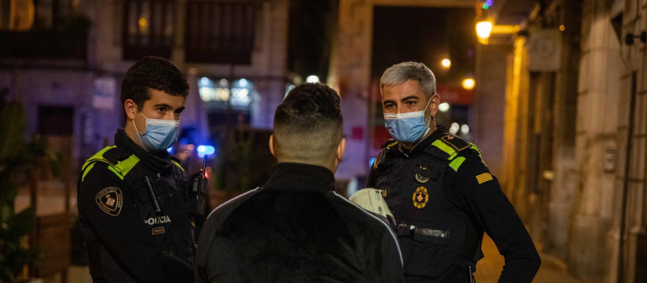 Una pareja de la Guardia Urbana multa a una persona tras la entrada en vigor del toque de queda, a 24 de diciembre de 2021, en Barcelona