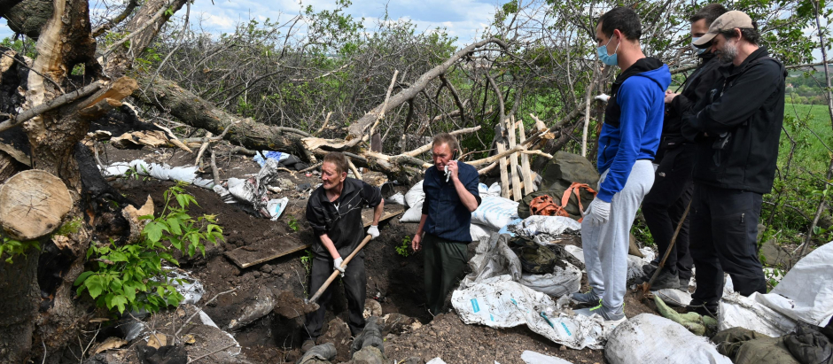 Residentes ucranianos ayudan a un médico forense a cavar una trinchera en Ucrania