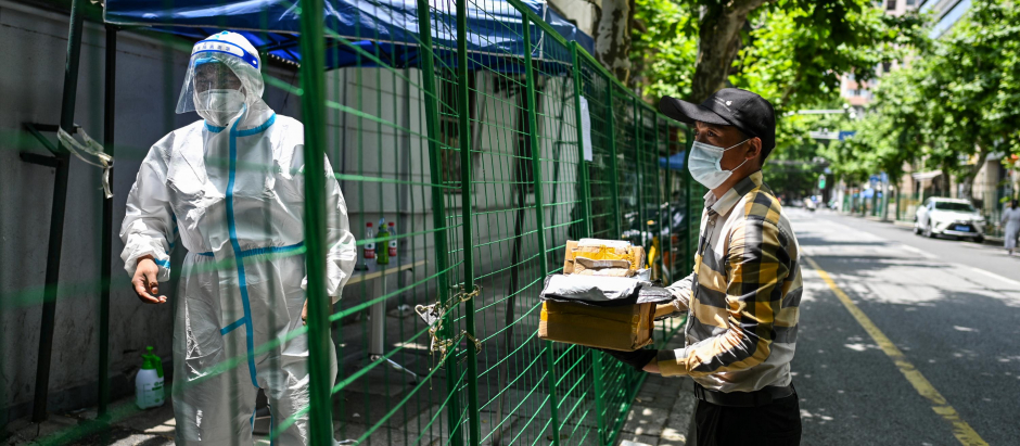 Un repartidor llega con un pedido mientras un trabajador con equipo de protección mira detrás de una cerca que asegura un área residencial bajo encierro por Covid-19 en el distrito Xuhui de Shanghái