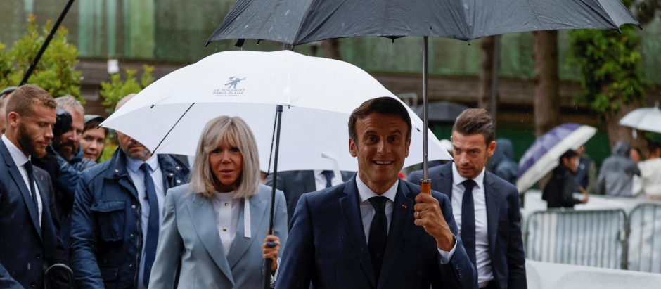 France's President Emmanuel Macron (C) walks with his wife Brigitte Macron (C/L) as he prepares to speak with onlookers as he leaves after casting his vote in the second stage of French parliamentary elections at a polling station in Le Touquet, northern France on June 19, 2022. (Photo by Ludovic MARIN / AFP)