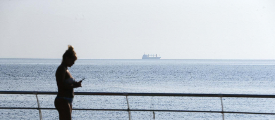 Dos personas toman el sol en el puerto de Odesa mientras se aleja un buque de carga con maíz ucraniano que ha zarpado de dicho puerto