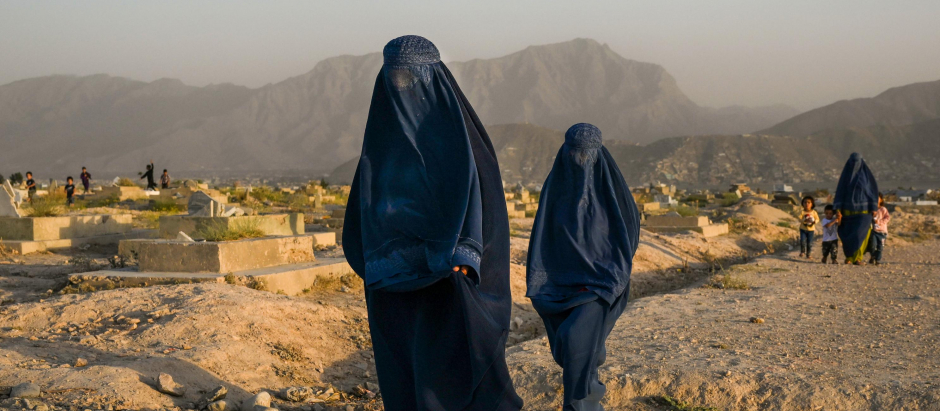 Mujeres afganas con burkas tradicionales pasan frente a un cementerio en Kabul