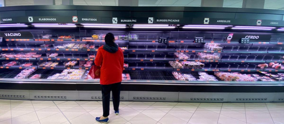 Una mujer observa los alimentos que quedan en los refrigeradores de carne de un supermercado un día marcado por colas de gente deseosas de hacer acopio de alimentos