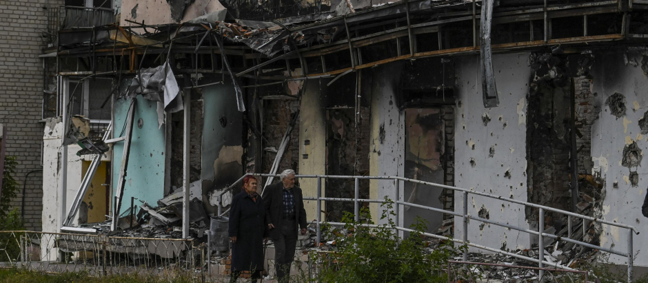 Dos personas caminan frente a un edificio en escombros en Izyum, región de Kharkiv