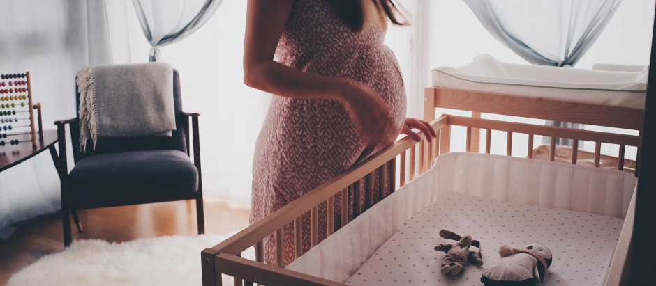 Una embarazada frente a la cuna preparada para su bebé