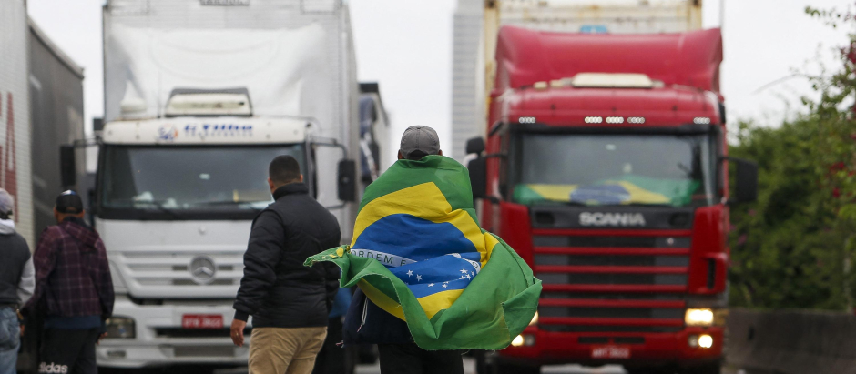 A supporter of President Jair Bolsonaro wears a Brazilian flag during a blockade on Castelo Branco highway, on the outskirts of Sao Paulo, Brazil, on November 2, 2022. - Bolsonarist supporters demonstrated again this Wednesday in Brazil, although the number of roadblocks decreased, after the announcement that Jair Bolsonaro authorized the transition to a new government of Luiz Inácio Lula da Silva. (Photo by Miguel SCHINCARIOL / AFP)
