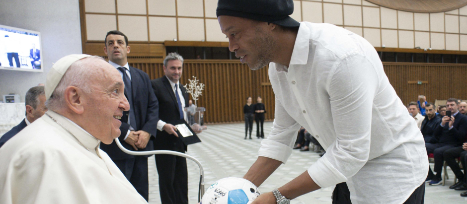 Former Brazilian player  Ronaldinho hands a football to Pope Francis during an audience to participants to a friendly tribute "match for peace" in memory of late Argentininan player Diego Maradona, on November 14, 2022 at Paul-VI hall in The Vatican. - The match is organised by "WePlayForPeace", a foundation set up by Pope Francis. (Photo by Handout / VATICAN MEDIA / AFP) / RESTRICTED TO EDITORIAL USE - MANDATORY CREDIT "AFP PHOTO / VATICAN MEDIA" - NO MARKETING NO ADVERTISING CAMPAIGNS - DISTRIBUTED AS A SERVICE TO CLIENTS