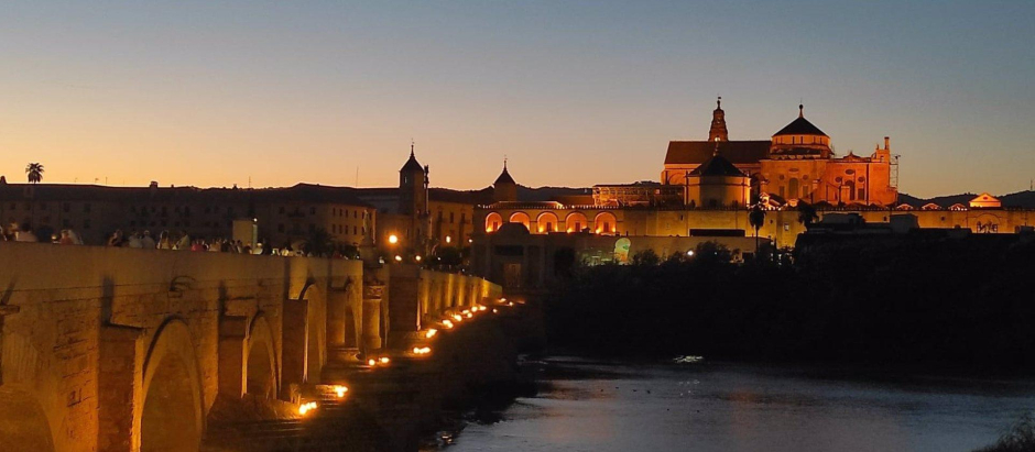 Turistas cruzan el Guadalquivir por el Puente Romano de Córdoba, con la Puerta del Puente y la Mezquita-Catedral al fondo