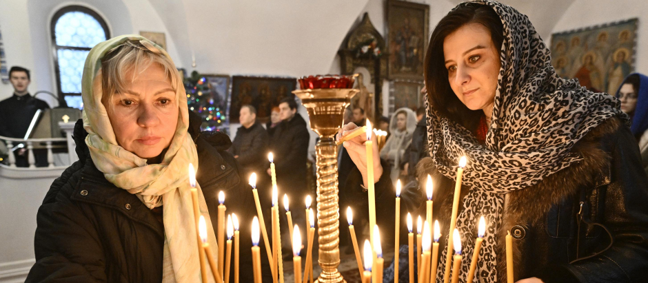 Women light candles during the Christmas service in a church of the Orthodox Church of Ukraine in Kyiv on December 25, 2022, amid the Russian invasion of Ukraine. - Church bells and Kyivan chanting rang throughout Ukraine's capital as Orthodox Christians attended Christmas services on December 25, 2022, a defiant break from Russian spiritual leaders who will mark the holiday in two weeks. The decision by some Ukrainian churches to observe Christmas on December 25 and not January 7, as is customary in Orthodox Christianity, highlights the rift between religious leaders in Kyiv and Moscow that has deepened with the ongoing war. (Photo by Genya SAVILOV / AFP)