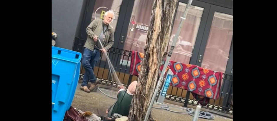 Un galerista rocía con una manguera a una mujer sin techo