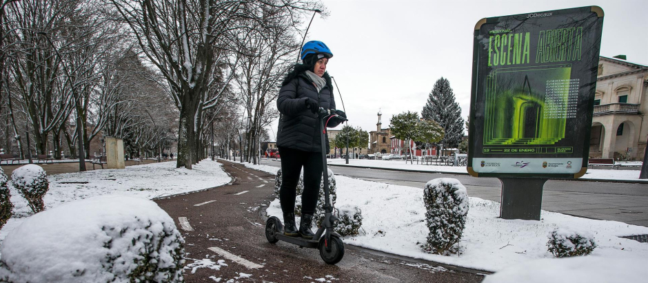 Una mujer conduce un patinete eléctrico por una calle cubierta de nieve