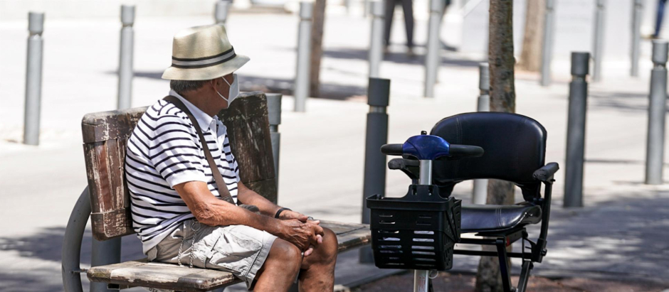 Un anciano con mascarilla sentado en un banco.