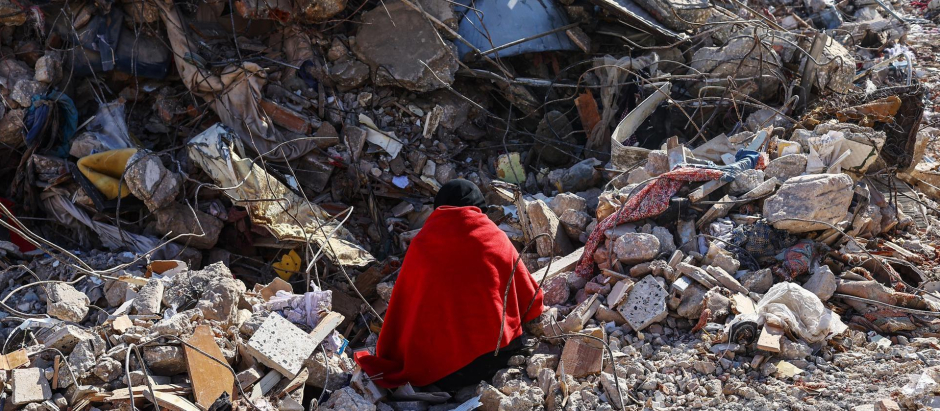 Una mujer sentada sobre los escombros de su casa