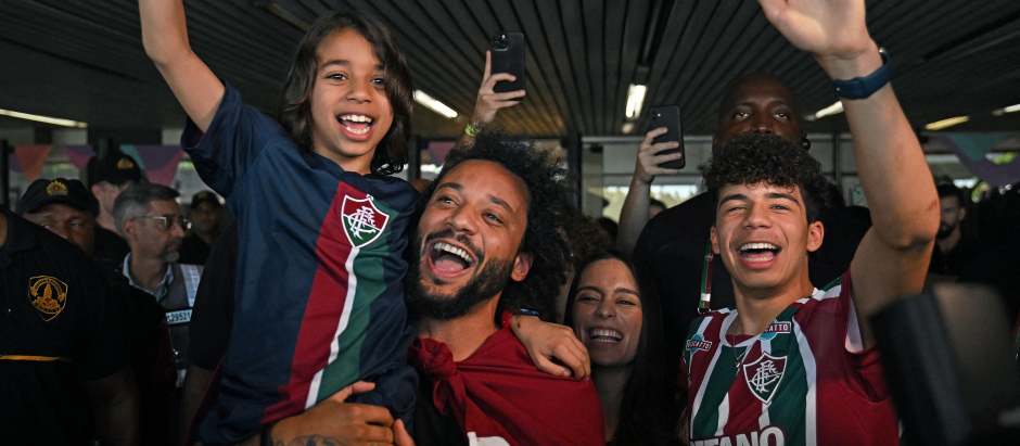 Brazilian defender Marcelo, wrapped in a flag of Brazilian team Fluminense, cheers at fans with his wife Clarise Alves and their sons Enzo (R) and Liam, upon arriving at Galeao Airport in Rio de Janeiro, Brazil, on March 9, 2023, on the eve of his official presentation. - Marcelo, five-time European champion with Real Madrid, signed with Fluminense until December 2024. (Photo by Carl DE SOUZA / AFP)