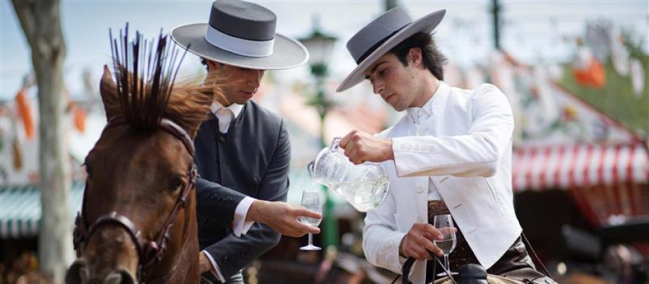 Dos personas se sirven un vaso de rebujito desde la jarra en la Feria de Abril de Sevilla