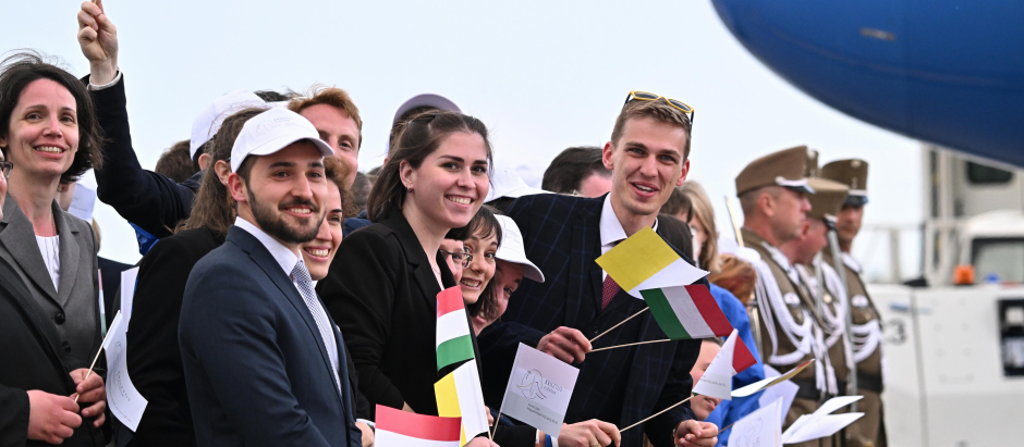 Un grupo de jóvenes ondea banderas italianas y del Vaticano durante la ceremonia de despedida del Papa Francisco en el Aeropuerto Internacional de Budapest