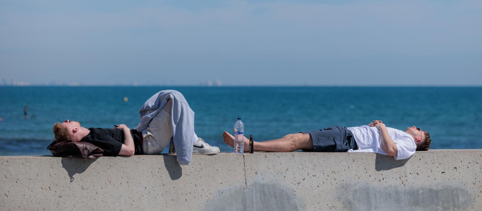 Dos personas descansan al sol en la playa de la Malvarrosa durante este segundo día de mayo en el que se mantienen las altas temperaturas