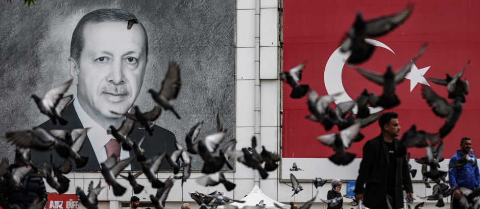 Personas pasan un retrato del presidente turco Recep Tayyip Erdogan y una bandera turca en Bursa, Turquía