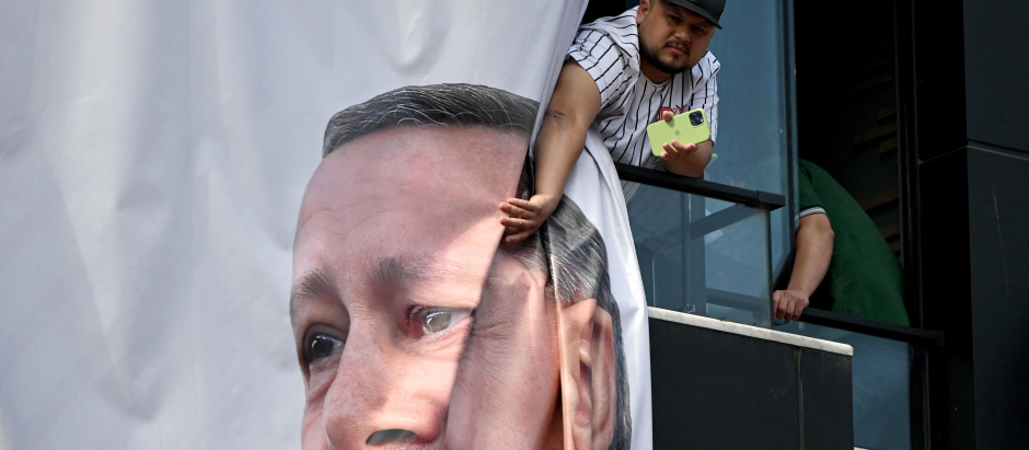A local resident watches the Turkish President's speech next to a banner with his portrait during a rally in the Beyoglu district on the eve of the presidential and parliamentary elections, on the European side of Istanbul, on May 13, 2023. Erdogan warned his conservative supporters they could face reprisals should his secular rival rise to power in momentous weekend polls. Erdogan has been trying to rally his base ahead of elections that put his Islamic style of rule in the largest Muslim-majority member of NATO on the line. (Photo by OZAN KOSE / AFP)