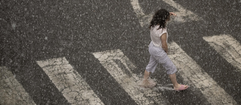 Una persona cruza en chanclas una calle bajo una fuerte tormenta que ha sorprendido este lunes a los vecinos de Ourense