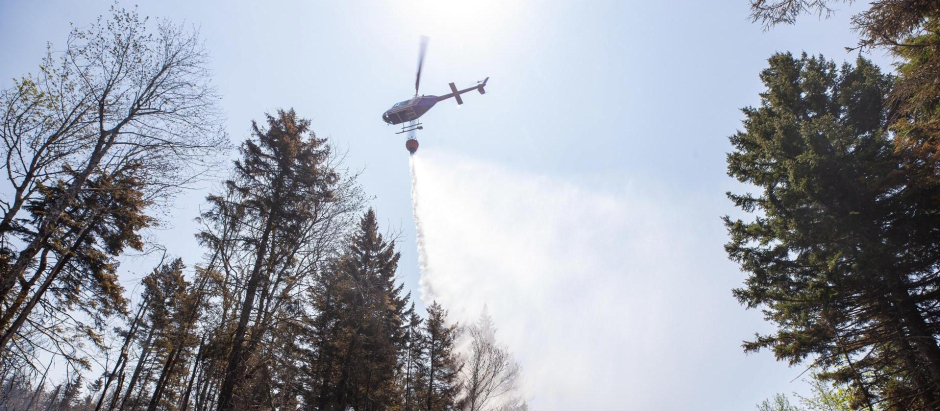Un helicóptero arroja agua mientras una excavadora hace un cortafuegos en el incendio forestal de Tantallon en Tantallon, Nueva Escocia, Canadá