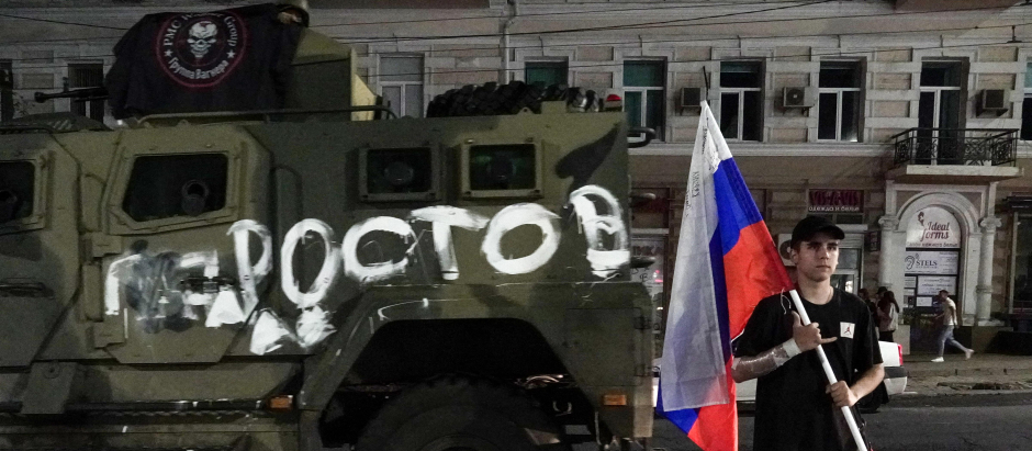 Un hombre sostiene la bandera nacional rusa frente a un vehículo militar del grupo Wagner con el cartel que dice Rostov