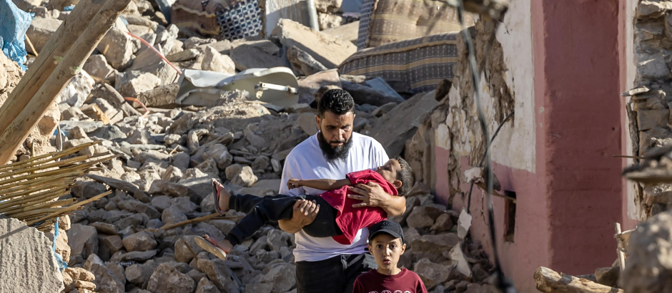 Un hombre carga a un niño mientras pasa junto a casas destruidas, en Marrakech