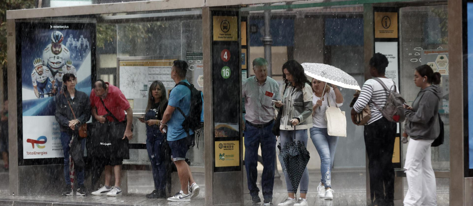 Un grupo de personas bajo la marquesina de un autobús se protegen de la lluvia en Pamplona