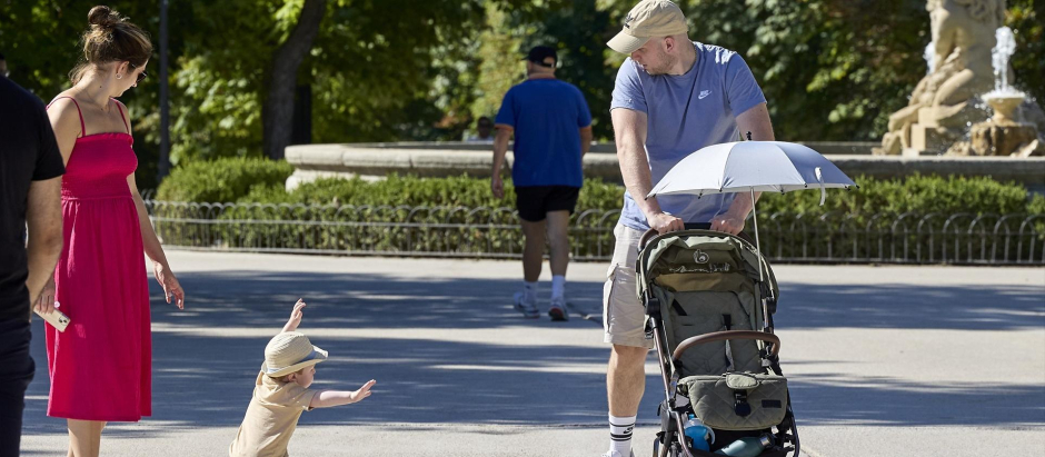 Varias personas pasean con un carrito de bebé en el parque de El Retiro.