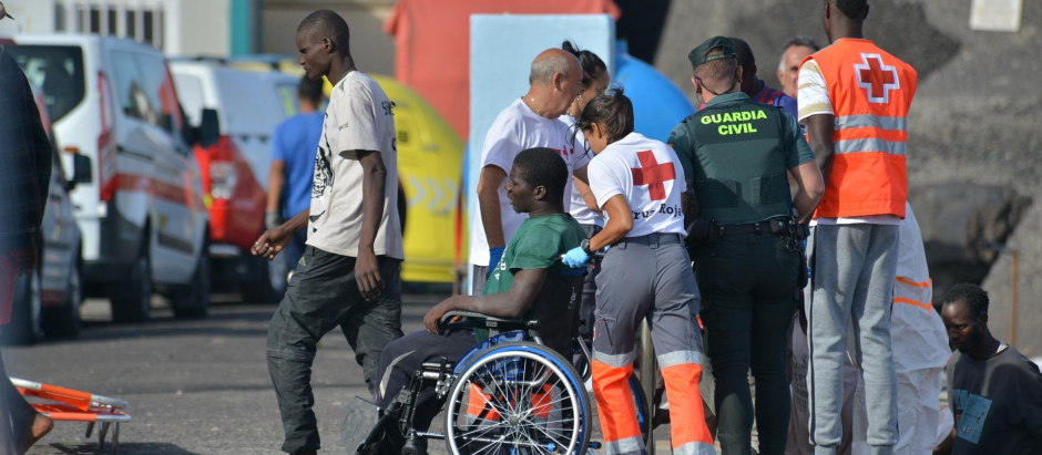 Una trabajadora de la Cruz Roja traslada en silla de ruedas a uno de los migrantes que ha llegado en un cayuco al puerto de La Restinga (El Hierro).