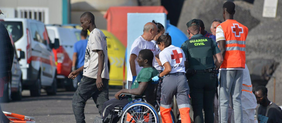 Una trabajadora de la Cruz Roja traslada en silla de ruedas a uno de los inmigrantes llegados en cayuco al puerto de El Hierro (Santa Cruz de Tenerife)