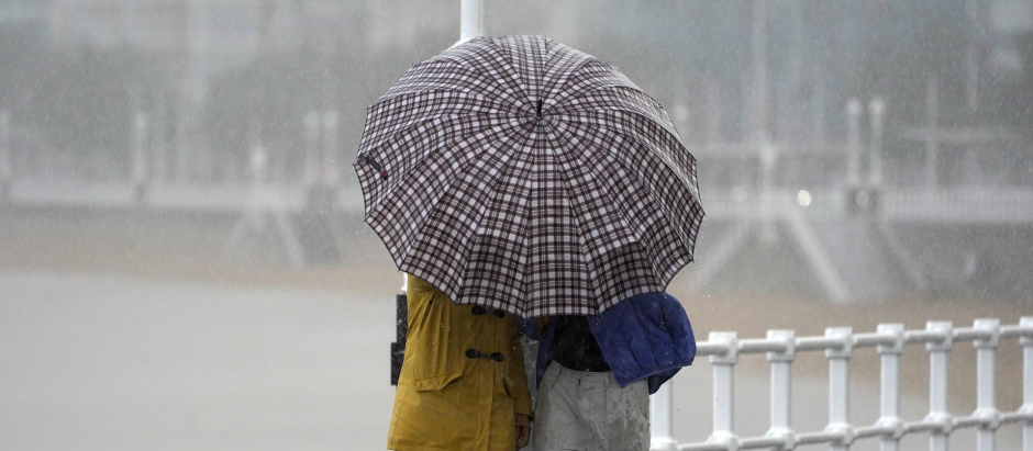 Dos personas comparten paraguas bajo la lluvia en la Playa de San Lorenzo de Gijón