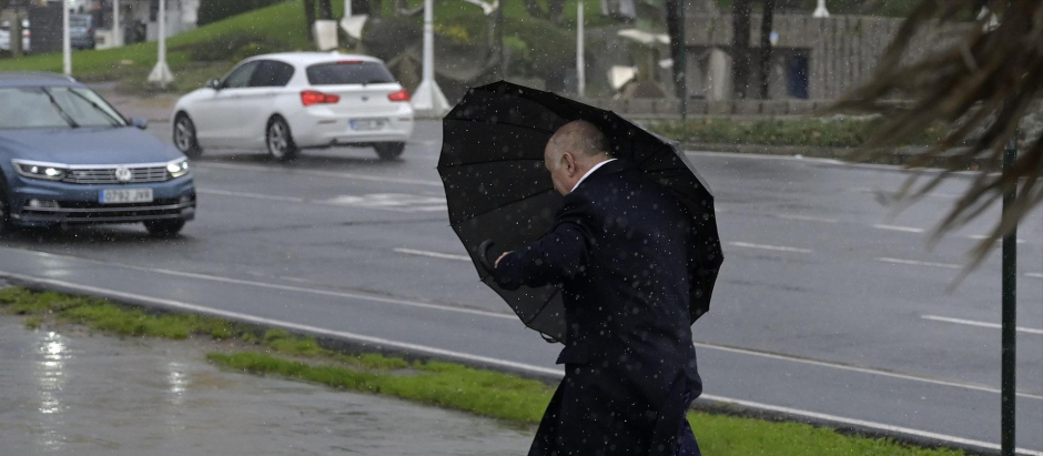 Un hombre con paraguas trata de refugiarse del viento y de la lluvia