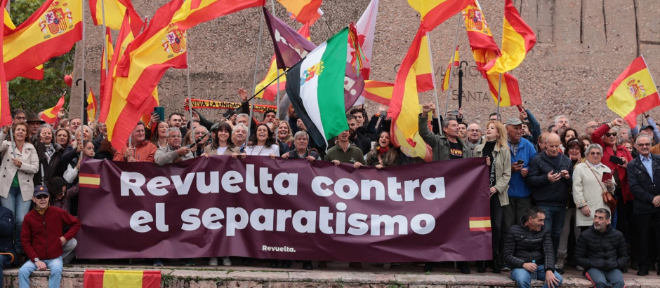 Varias personas junto a la pancarta de 'Revuelta' en la manifestación de DENAES en Colón contra la amnistía