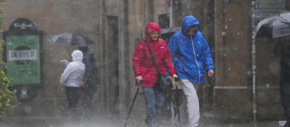 Varias personas con ropa para la lluvia esta mañana en el casco histórico de Santiago de Compostela