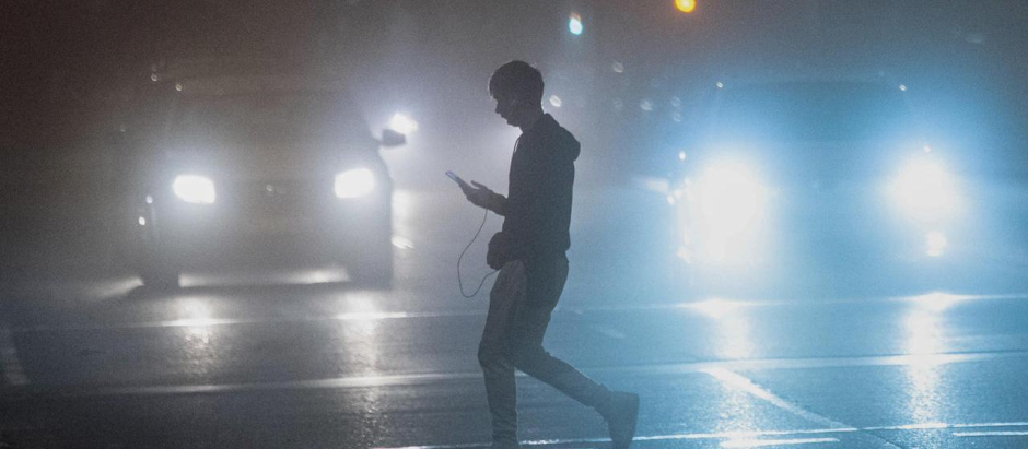 Un joven cruza una calle bajo un banco de niebla que se ha formado al final del día de este domingo en Castellón