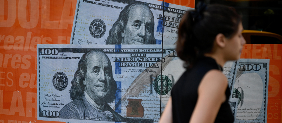 Una mujer pasa junto a una imagen de billetes de cien dólares estadounidenses en Buenos Aires