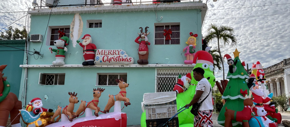 Un hombre tira de un carrito mientras pasa junto a una casa con adornos navideños inflables, en La Haban