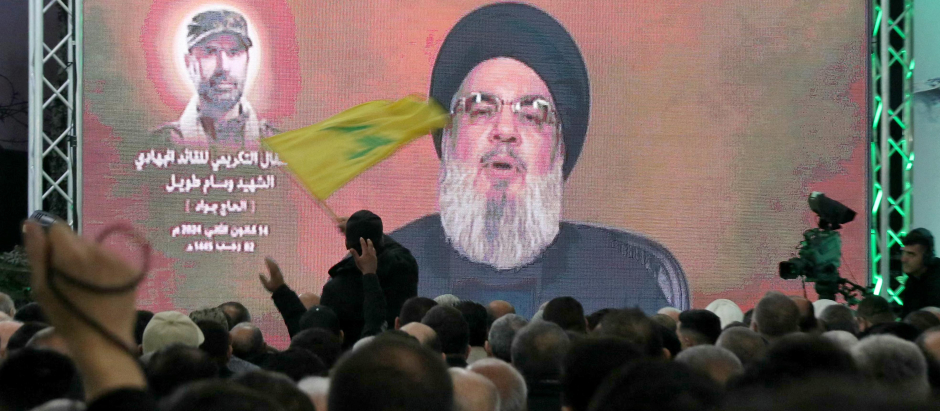 Un hombre ondea una bandera del movimiento Hezbolá mientras su líder, Hassan Nasrallah, pronuncia un discurso televisado