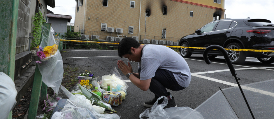 Hombre rezando junto a flores y tributos colocados en el lugar donde 36 personas murieron en un incendio en el edificio de una empresa de animación en Kioto.