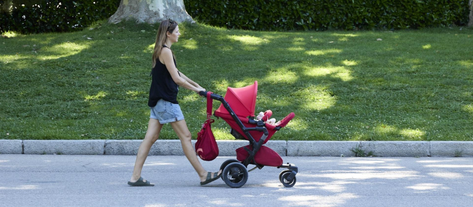 Una mujer pasea con un carrito de bebé en el parque de El Retiro