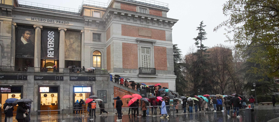 Decenas de personas con paraguas hacen cola en el exterior del Museo del Prado para realizar una visita de noche