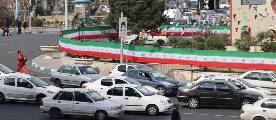 Los automóviles pasan junto a una pared cubierta por una pancarta con los colores de la bandera nacional en Teherán