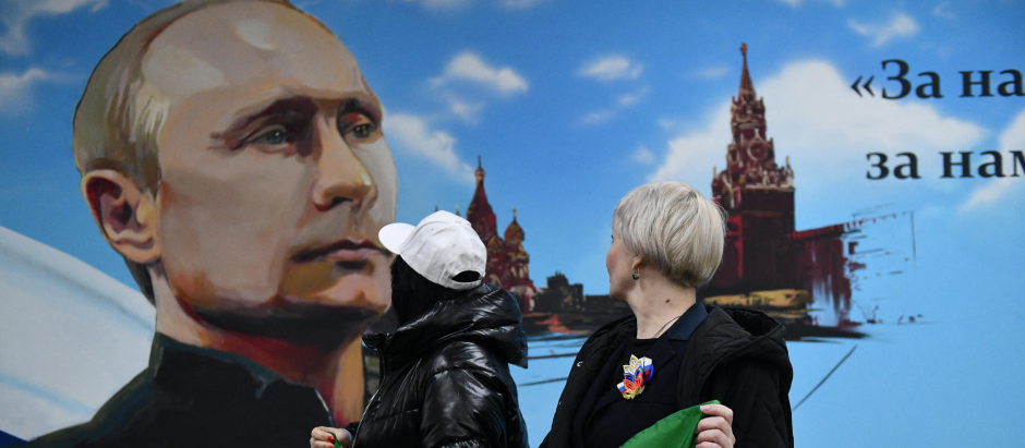 Mujeres posan frente a un mural que representa al presidente ruso Vladimir Putin después de votar en las elecciones presidenciales de Rusia