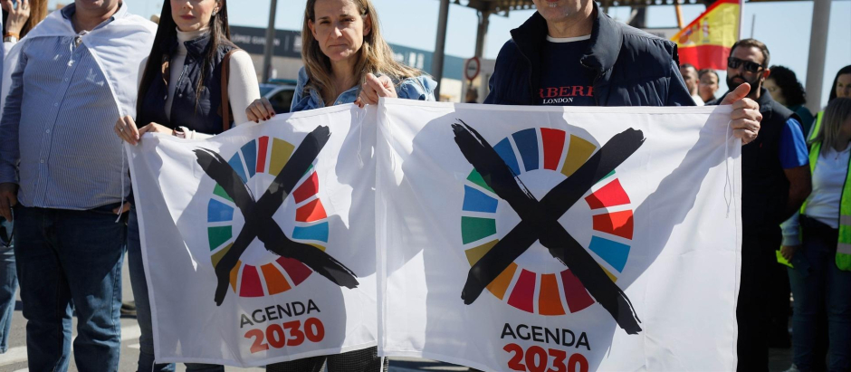 Varias manifestantes con banderas de la Agenda 2030 tachadas