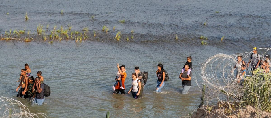 Inmigrantes caminan entre alambre de concertina y una serie de boyas colocadas en el agua a lo largo de la frontera del río Grande con México en Eagle Pass, Texas