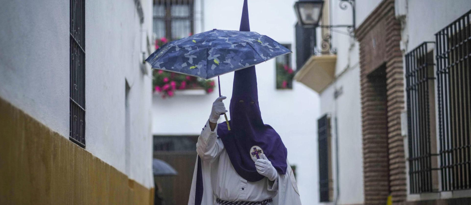 Un nazareno de la Hermandad de La Pasión se cubre con un paraguas el Miércoles Santo a la espera de la suspensión por lluvia de su estación de penitencia