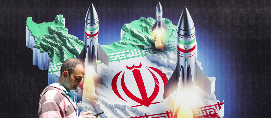Un hombre pasa junto a una pancarta que representa misiles lanzados desde Irán, en Teherán