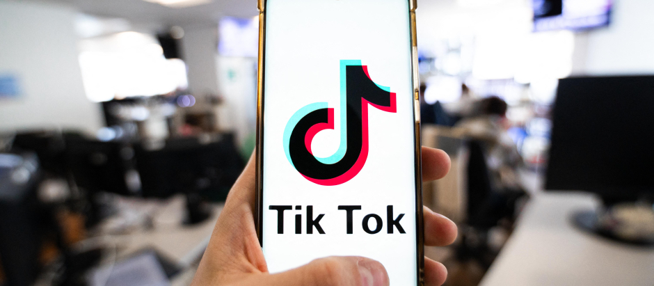 Un hombre sosteniendo un teléfono inteligente con el logotipo de la plataforma china Tiktok en una oficina en París